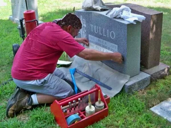 Stonesmith carving a name into an existing headstone, on-site in a New England cemetery